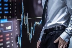Business man crossing his fingers on top of stock market numbers and graph